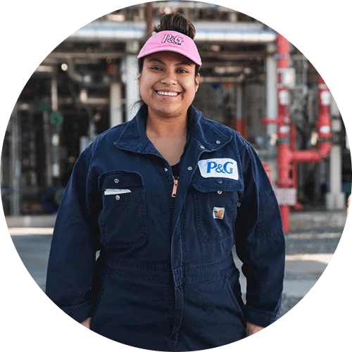 Woman smiling in a manufacturing facility, wearing a pink visor, dark blue jumpsuit with P&G logo.