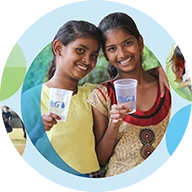 Two smiling girls standing next to each other hold clear cups with the "P&G" logo on them. The background includes overlapping light blue and green circles, creating a layered effect. A blue circle outline surrounds the icon.