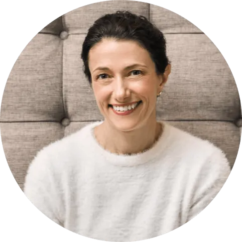Smiling woman with dark hair pulled back, wearing a white jumper, looking directly at the camera.