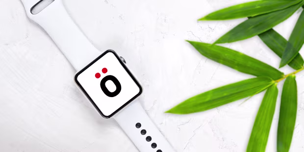 Refurbished Smartwatch, umgeben von Pflanzen auf hellem Hintergrund