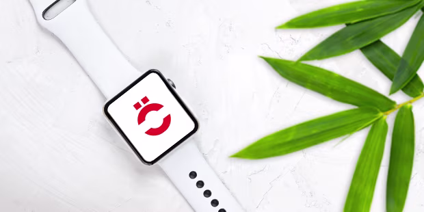 Refurbished Smartwatch, umgeben von Pflanzen auf hellem Hintergrund