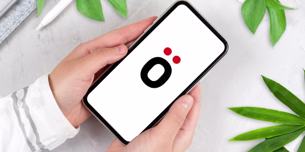 Hände die ein refurbished Smartphone halten, umgeben von Pflanzen auf hellem Hintergrund