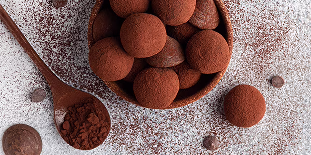 Mit Kakao bedeckte Rumkugeln in einer Schüssel auf mit Staubzucker bedecktem Hintergrund