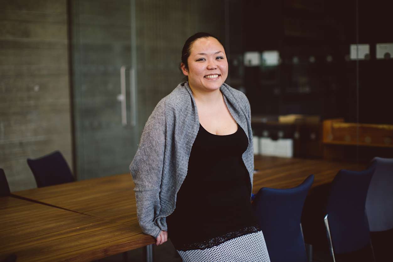 Professional woman stands in board room, smiling to camera.