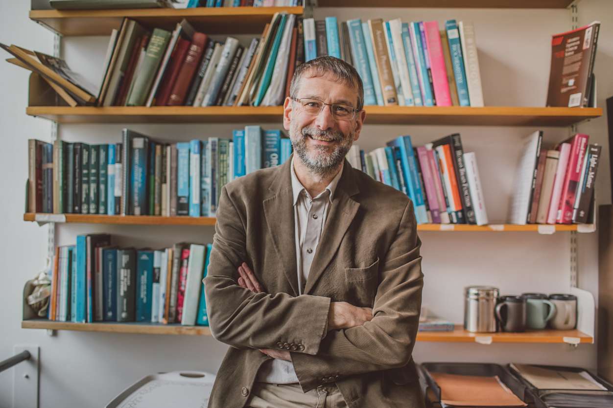 Man, smiling, looking to camera, standing in front of a large bookshelf