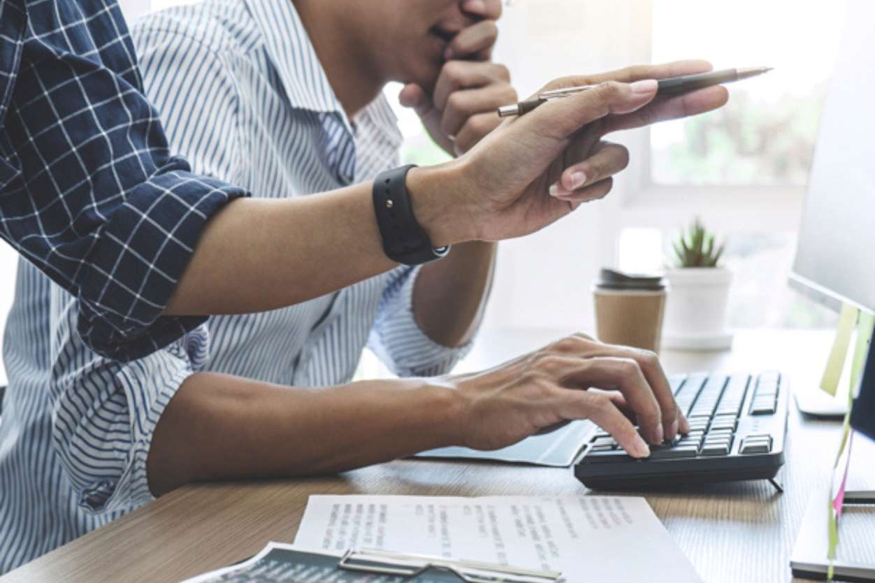 Close up of two individuals working at a desk and computer