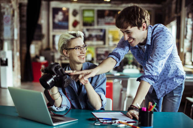 Close up of two young graphic designers checking photos on a camera and laughing.