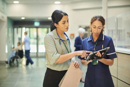 Healthcare Worker talking to a colleague and looking at a medical chart.