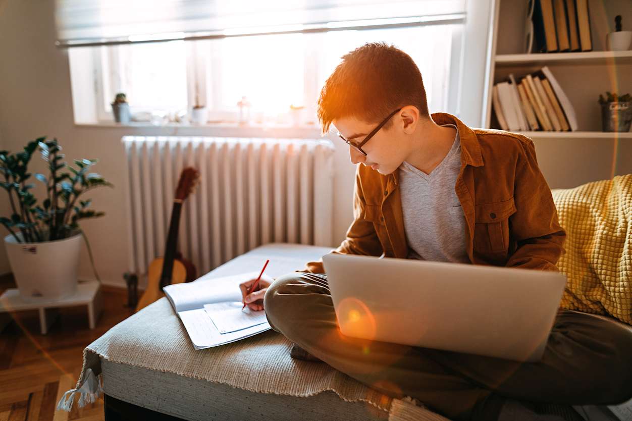 Student sits on bed working at computer