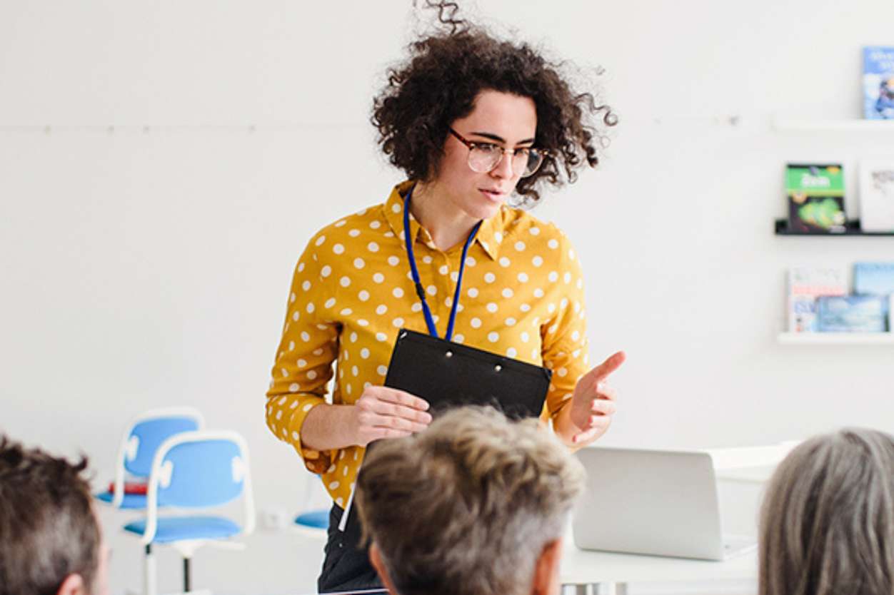 Image of professional leading a workshop, holding a clipboard in front of an audience.