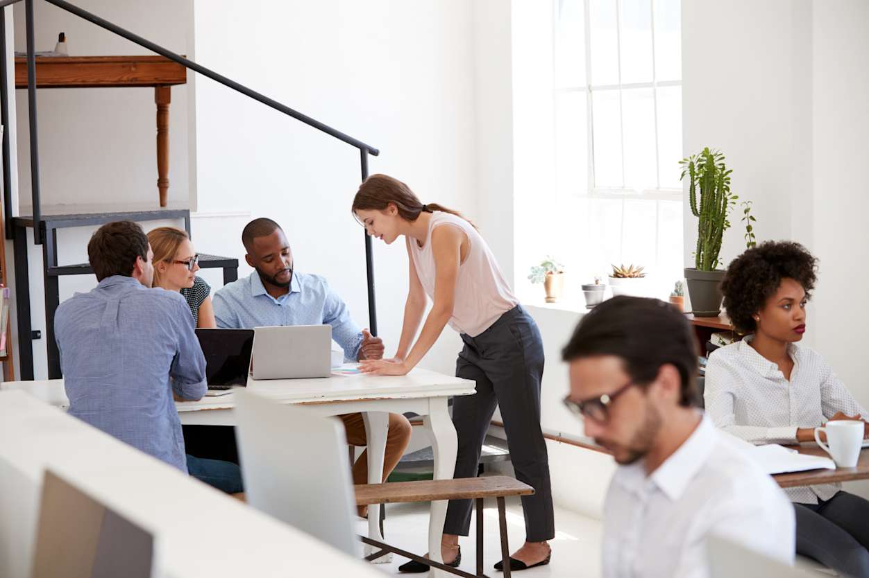 Image of office with various professionals working at desks or in discussion.