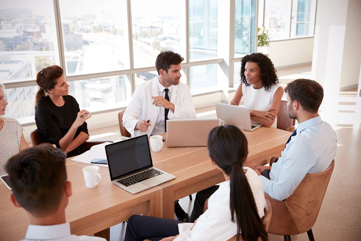 Group of professionals sit around a table chatting and working on laptops