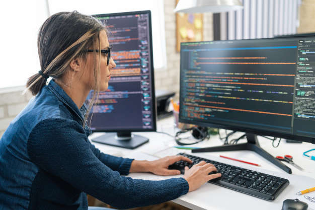 Woman sits at a computer which displays coding