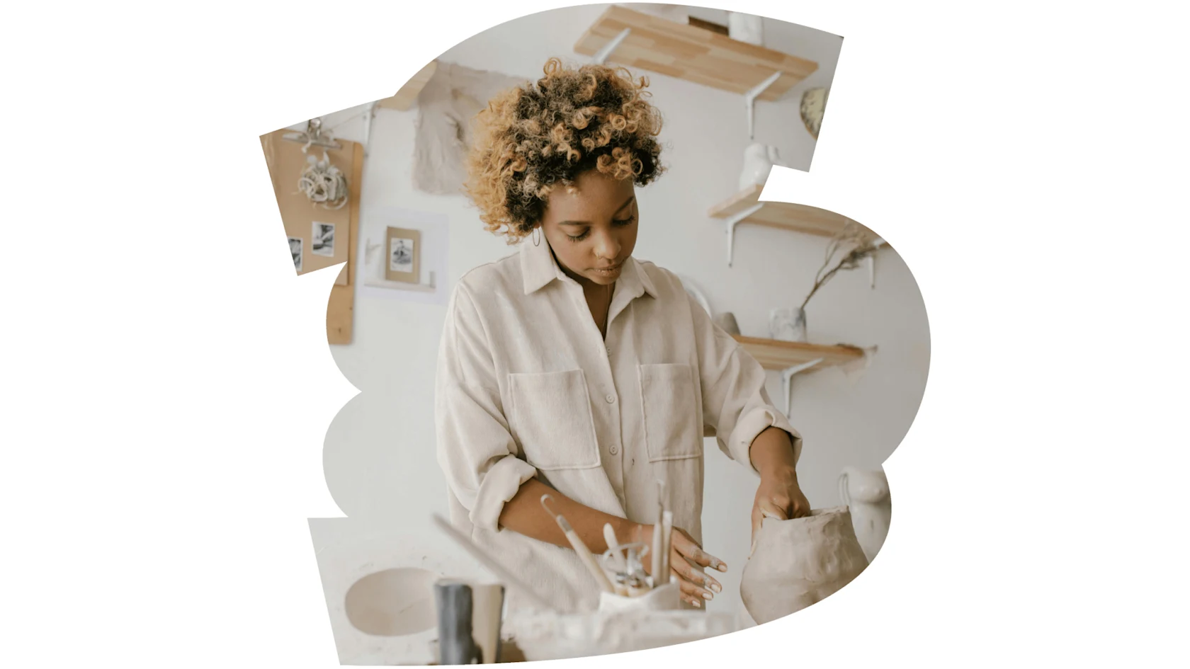 A woman in a pottery studio uses her hands to shape a clay vase