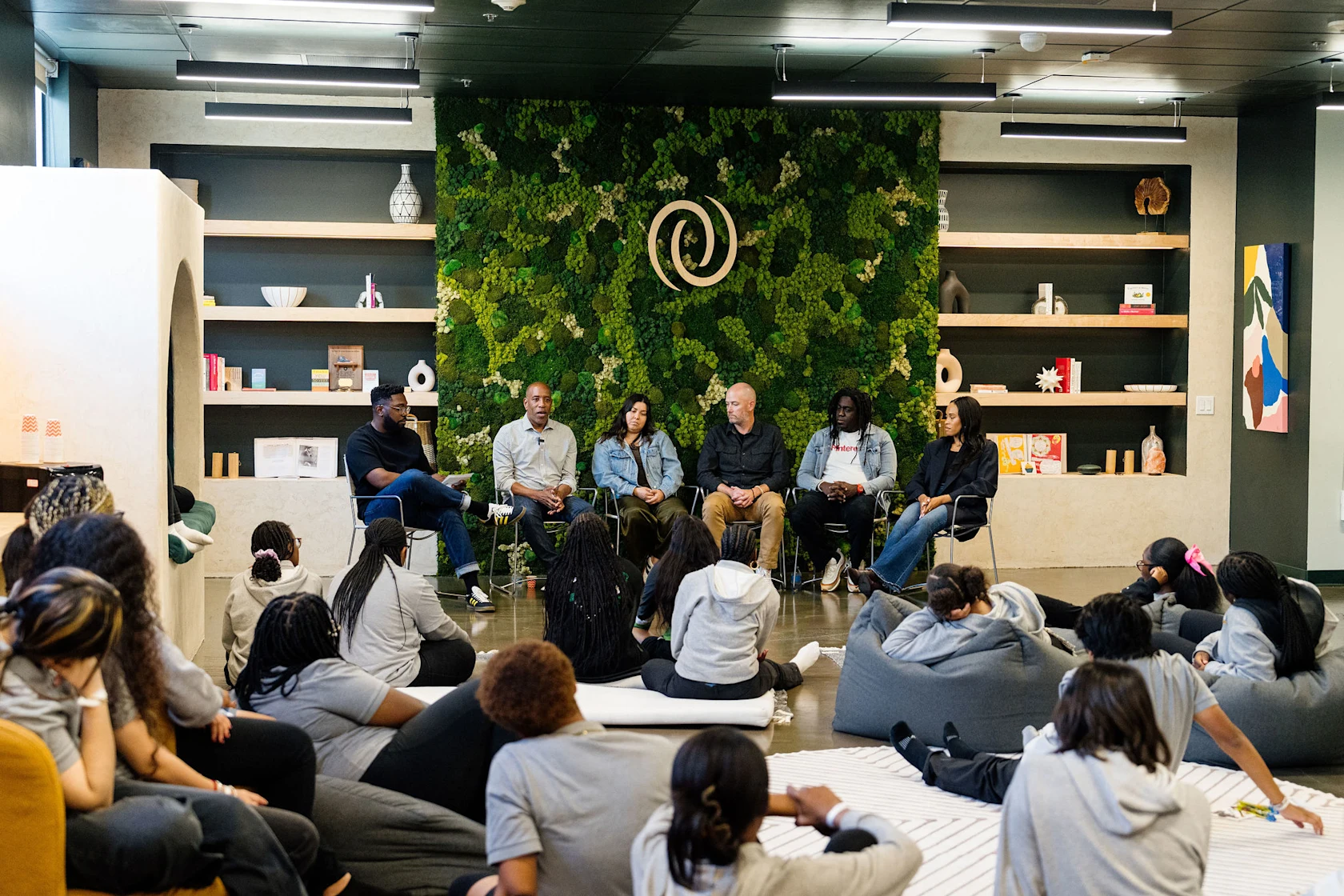 Four volunteers speaking on a panel with moderator, students in audience