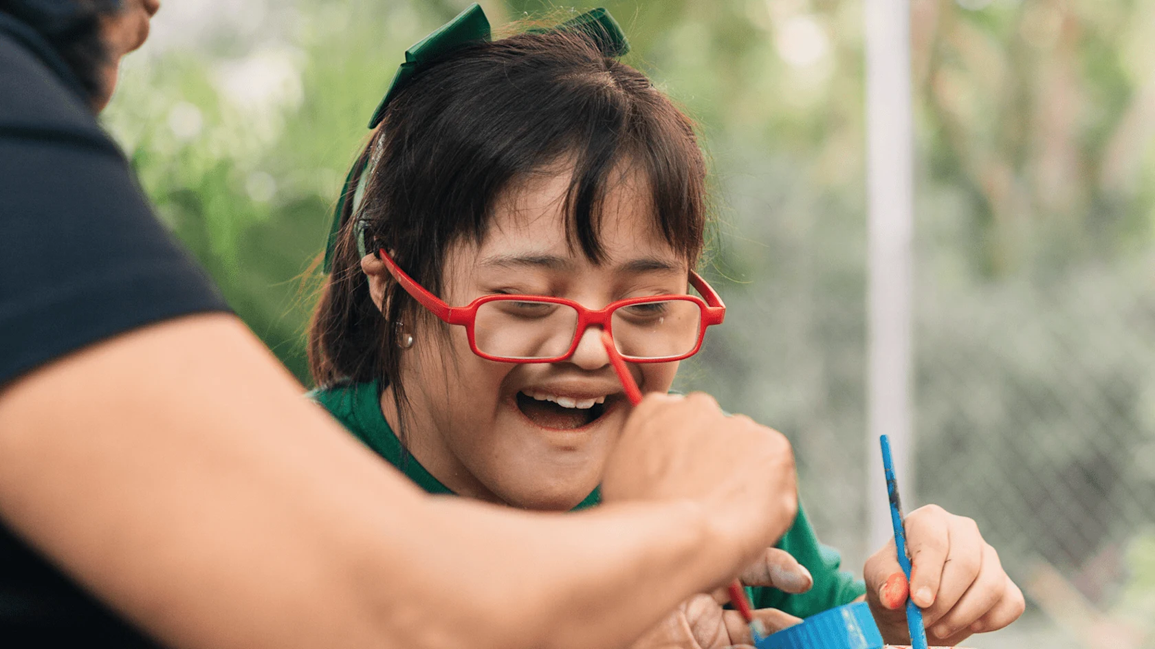 Enfant faisant une activité manuelle avec un adulte en plein air.