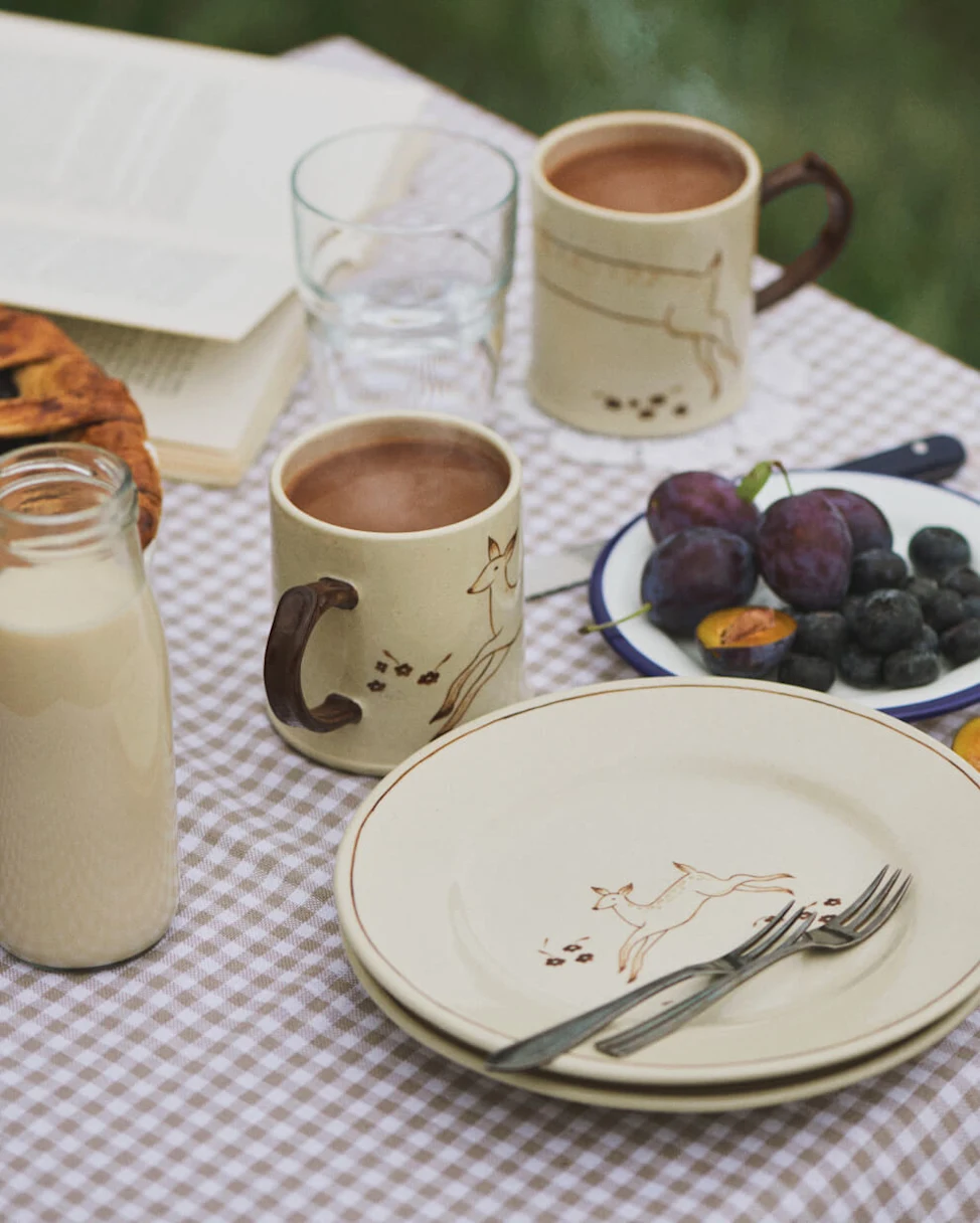 Cosy outdoor picnic with coffee, pastries, fruit, and nature-inspired tableware.