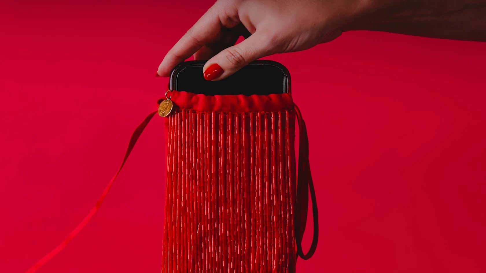 Phone being placed in red phone-free beaded silk bag by woman’s arms with red nails