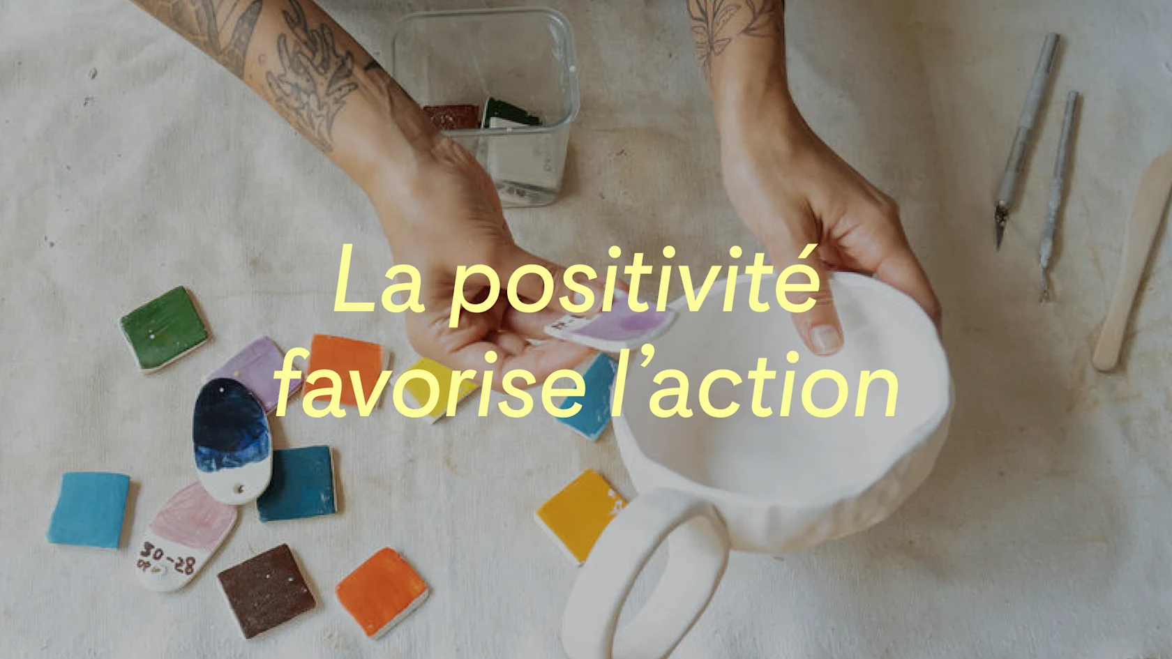 Céramiste testant différents échantillons de couleurs sur une tasse fabriquée à la main, avec les mots « La positivité favorise l’action » superposés sur l’image