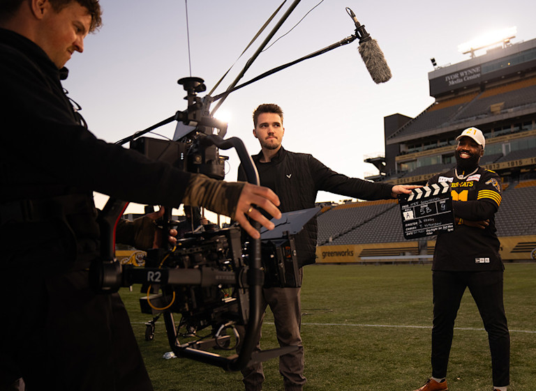 Oak + Rumble crew slating a take on a stadium field at sunset, with a gimbal camera rig and boom mic in the foreground