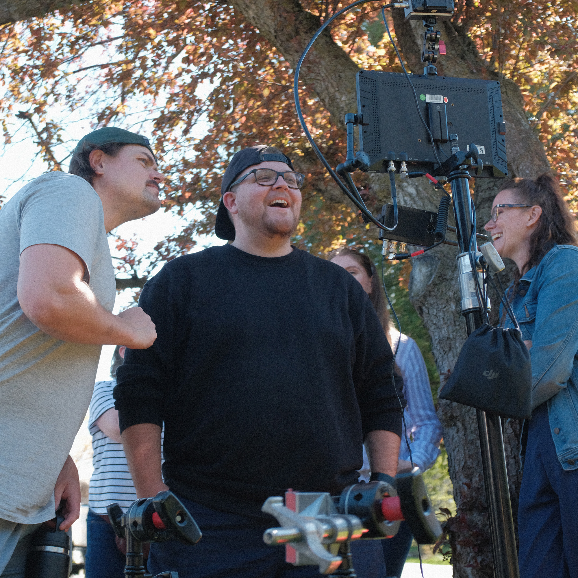 Oak + Rumble crew and client team laughing around a field monitor during an outdoor video shoot