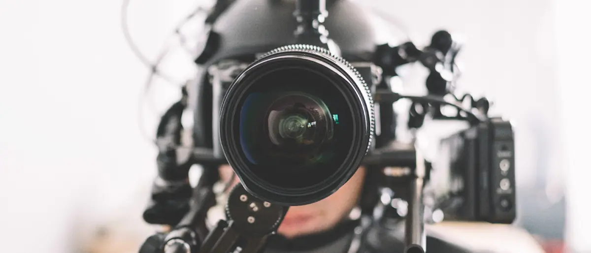 Crew member wearing a POV helmet camera rig with a wide cine lens and follow focus, facing the camera.