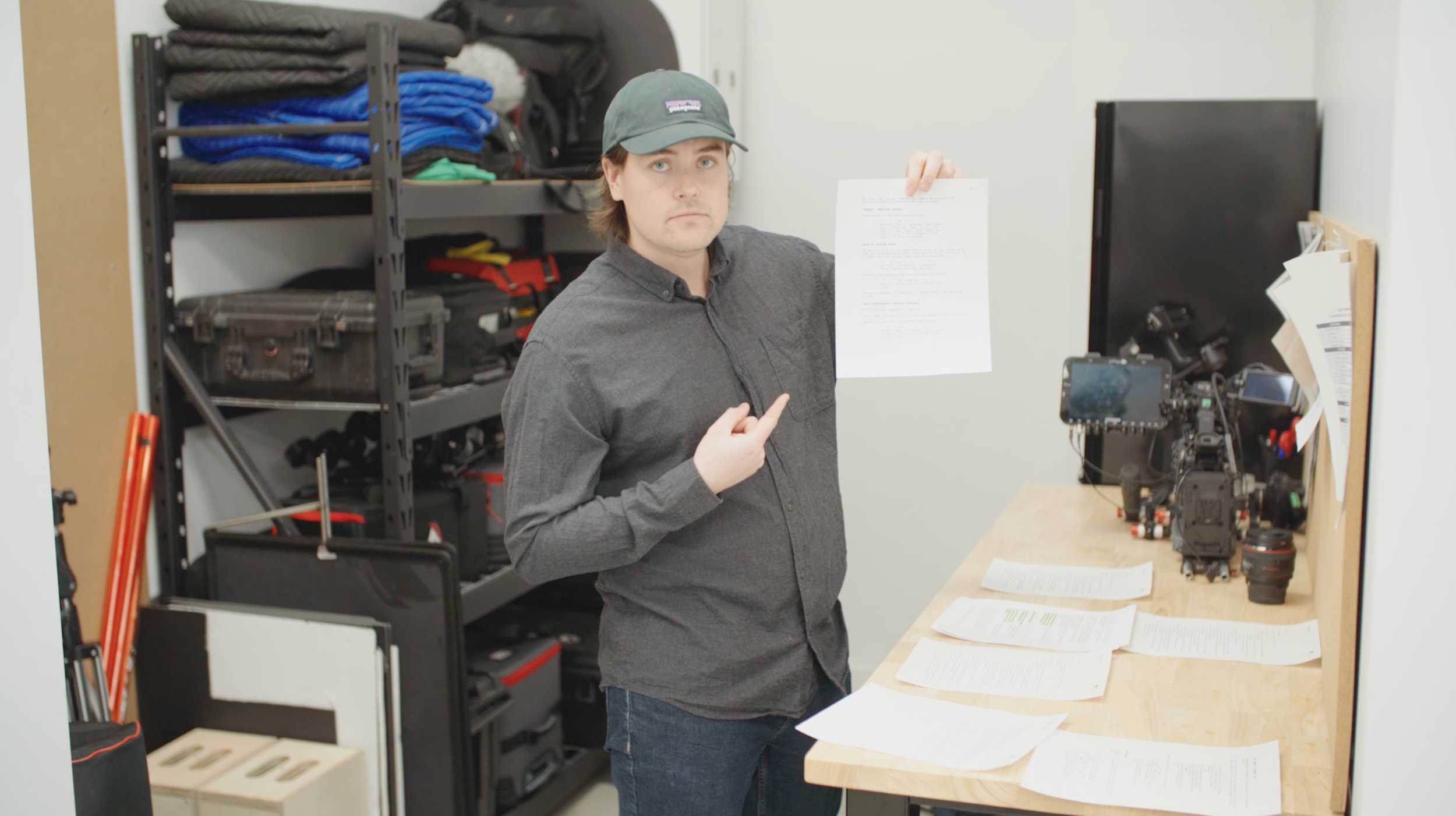 Dave Hiff holds up a script in the Oak + Rumble gear prep bay, with a camera and pre-production documents on the bench.