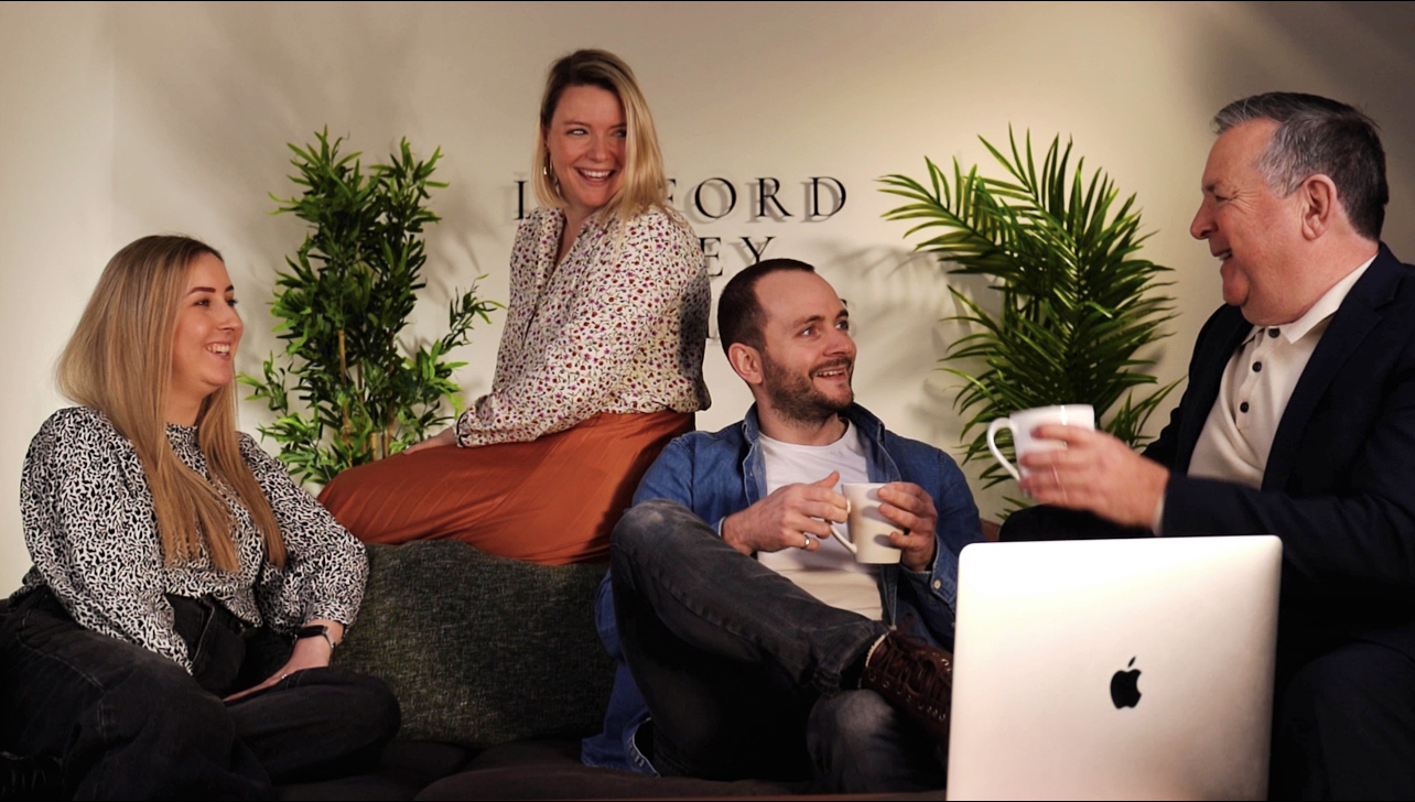 The Linford Grey team are sitting on a sofa together, laughing and drinking cups of tea.