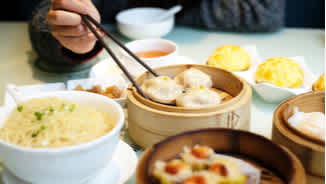 Person eating Chinese dumplings and dim sum with chopsticks at Cantonese restaurant in London