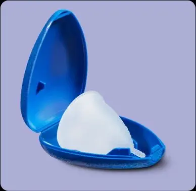 En el envase azul abierto se encuentra una copa menstrual blanca y ligeramente transparente. Se puede ver su cara exterior.
