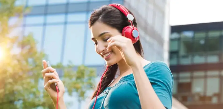 Una mujer sonriente en la ciudad escuchando música con auriculares