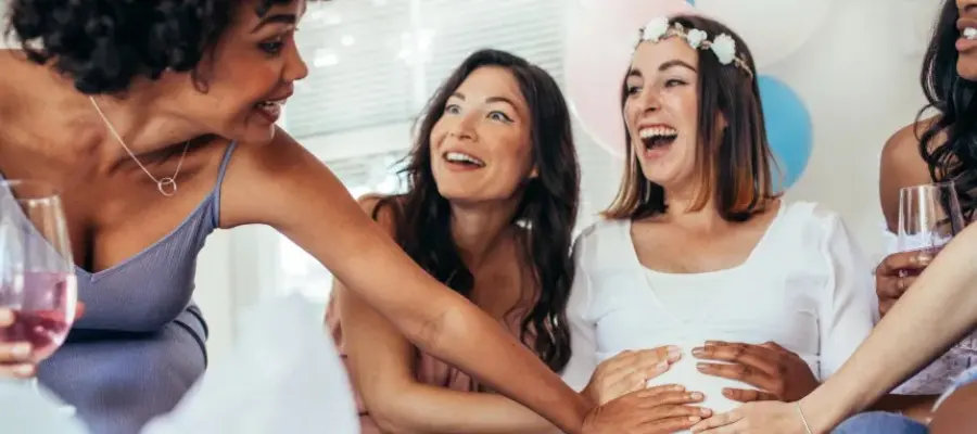 Mujeres riendo y tocando el vientre de una amiga embarazada en un baby shower