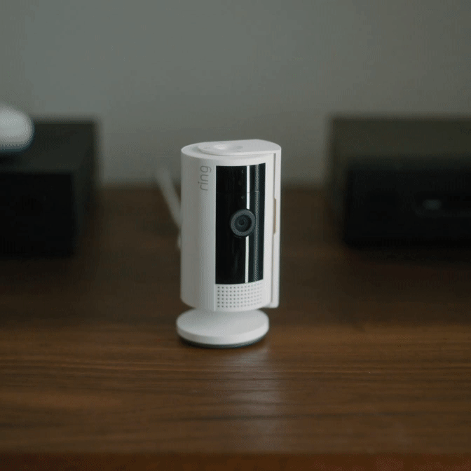 Hand closes Ring Indoor Camera's privacy cover; app confirms camera and mic are turned off for full control.