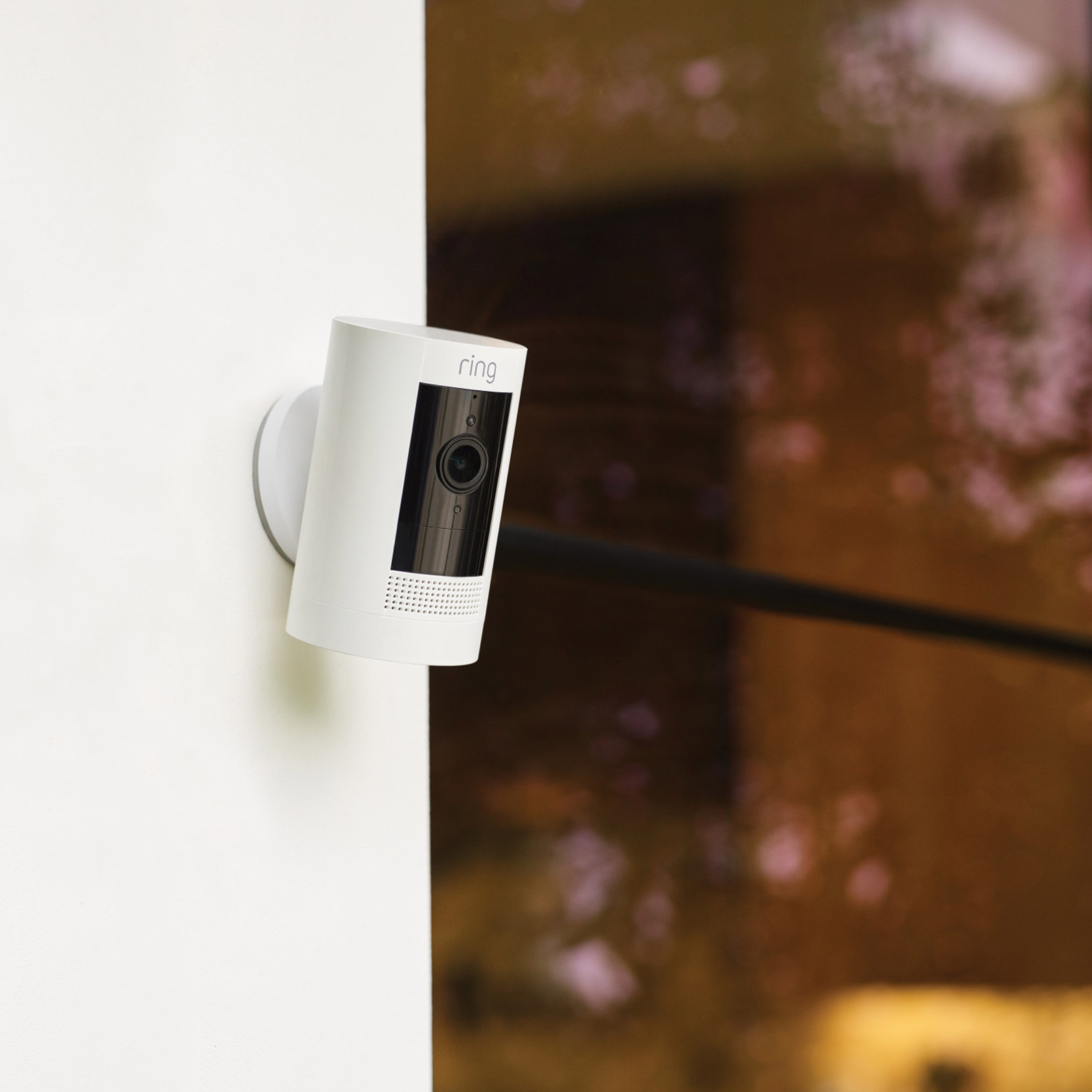 White Ring security camera mounted on an exterior wall, with a reflective glass surface in the background.