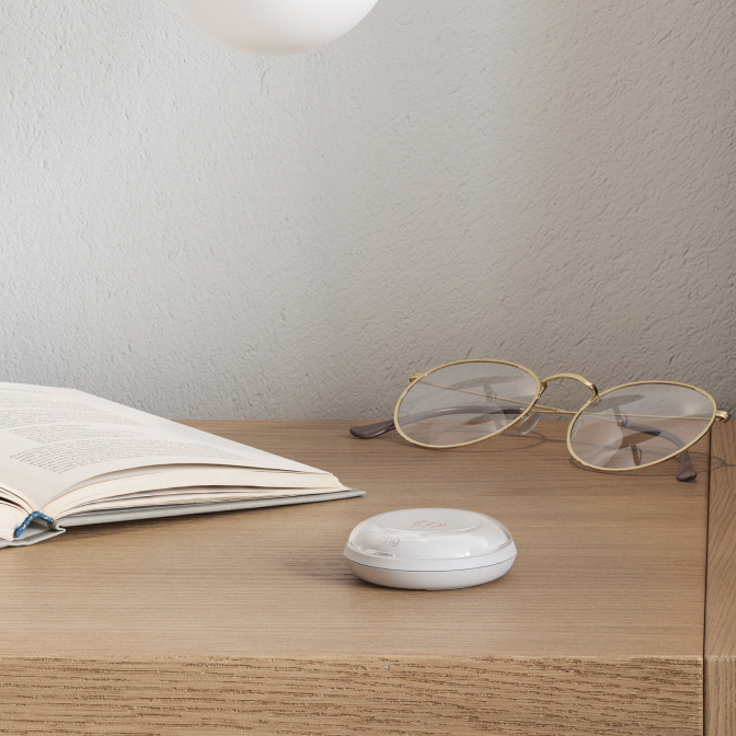 Ring Panic Button placed on a wooden bedside table beside an open book and glasses for quick emergency access.