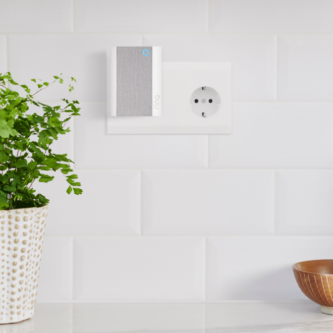 Ring Chime plugged into wall socket on white tile backsplash, beside potted plants and a wooden bowl.
