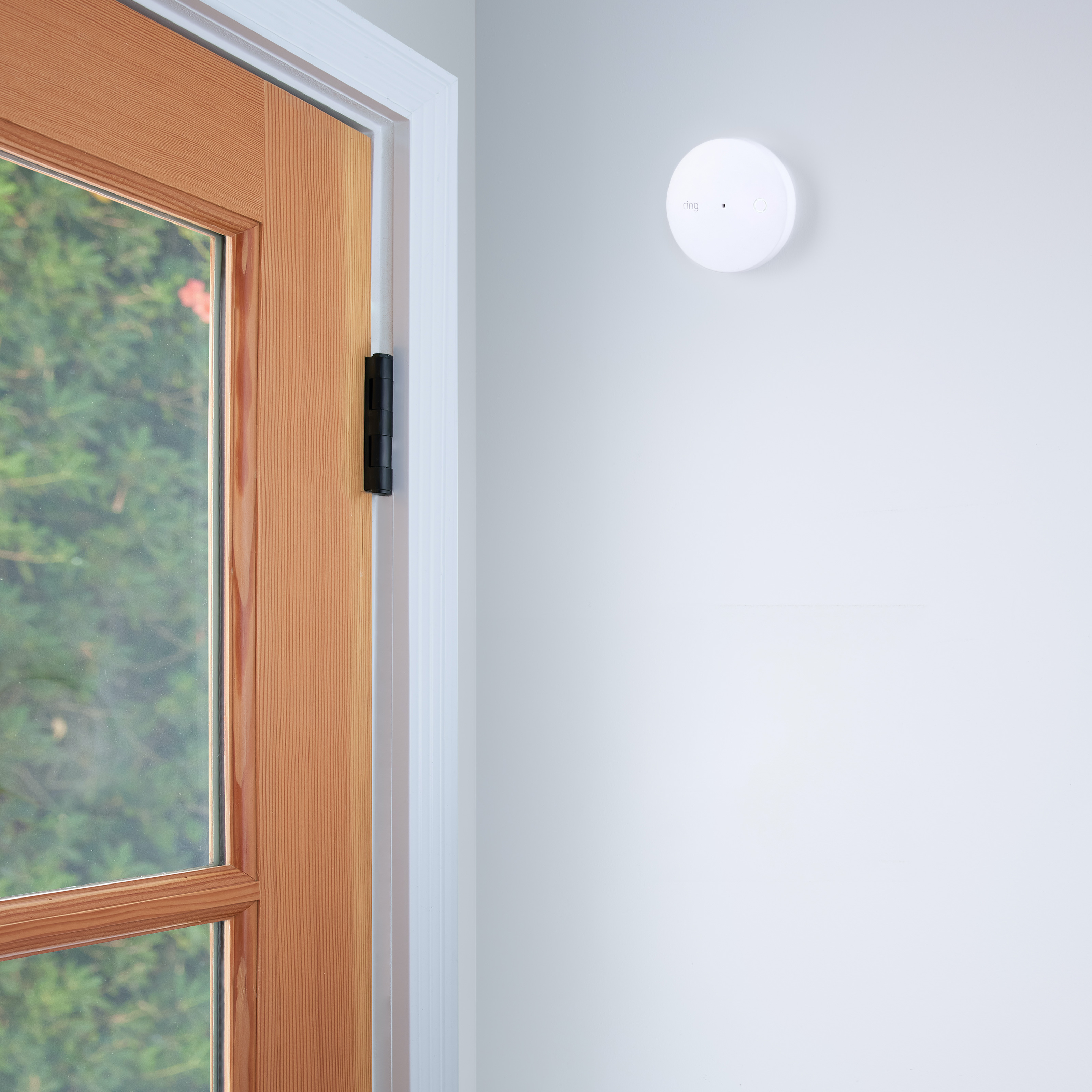 Ring Alarm Glass Break Sensor mounted on wall near wood-framed glass door for detecting sound of breaking glass.