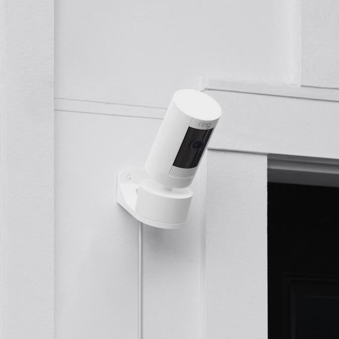 White Ring Stick Up Cam with Pan-Tilt Mount installed on an exterior wall, angled downwards for outdoor monitoring.