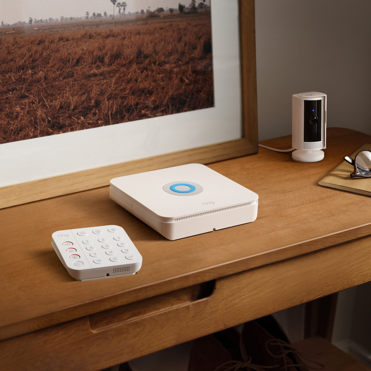 Ring Alarm Security System with keypad, base station, and indoor camera on a desk next to keys, glasses, and a notebook.