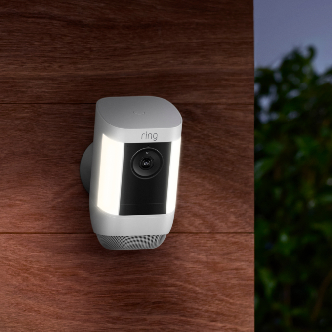 Ring Spotlight Cam Pro with dual LED lights and camera, wall-mounted on wood surface for advanced outdoor security.