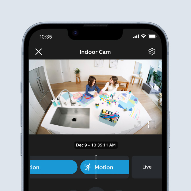 Ring app on phone shows Indoor Cam recording two children crafting at a kitchen table on 9 Dec at 10:35 a.m.