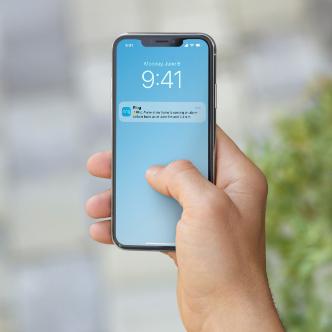 Hand holding phone showing Ring alert about Alarm running on cellular backup, with the time and date.
