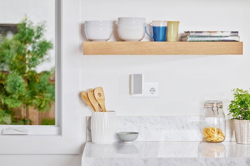 Ring Chime Pro plugged into kitchen wall socket beneath shelf with bowls, mugs, and next to wooden utensils on counter.