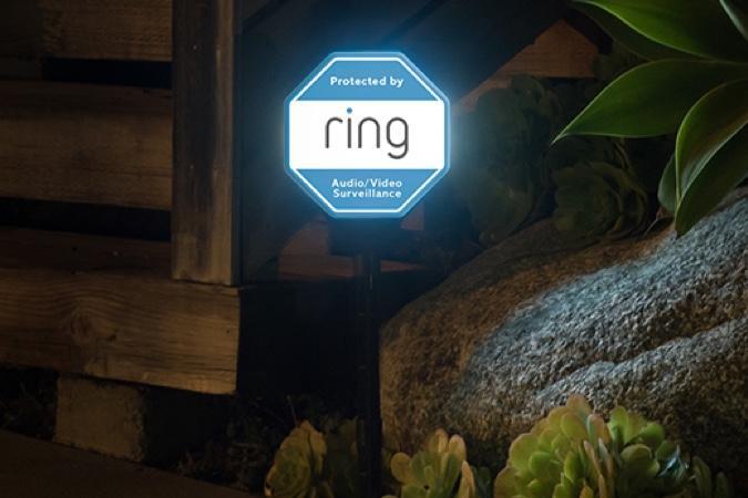 Illuminated Ring Solar Security Sign in a garden at night, indicating home protection with audio and video surveillance.