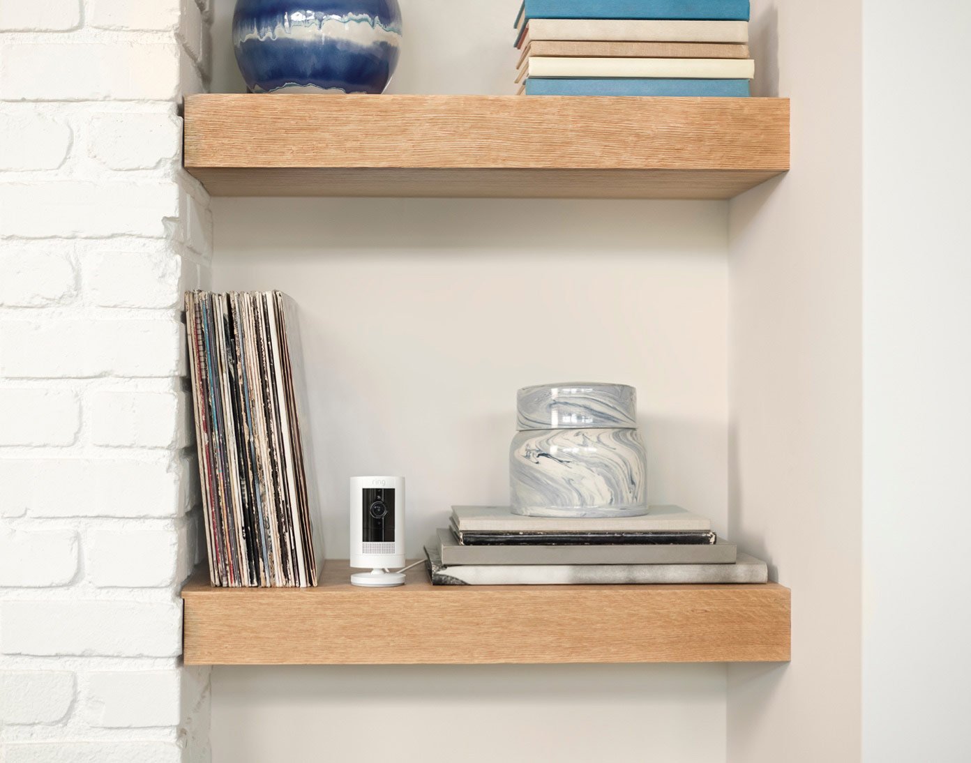 Ring Stick Up Cam op een plank naast boeken en decoratie in een woonkamer.