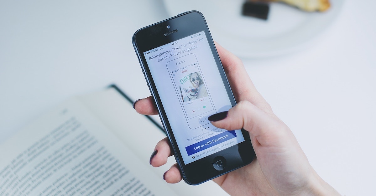 Mão de mulher utilizando o Tinder em sua tela inicial, que exige login com Facebook - Facebook cursos