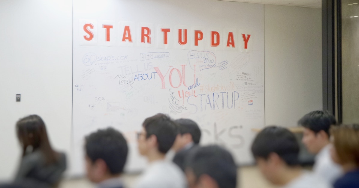 Pessoas em uma sala e, ao fundo, um quadro branco em que está escrito Startup Day