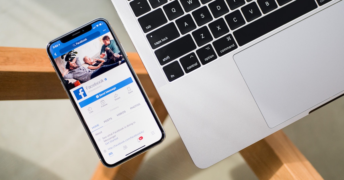 Foto de um laptop ao lado de um celular, que está aberto na página de uma empresa no Facebook - Conheça boas práticas de redes sociais para negócios