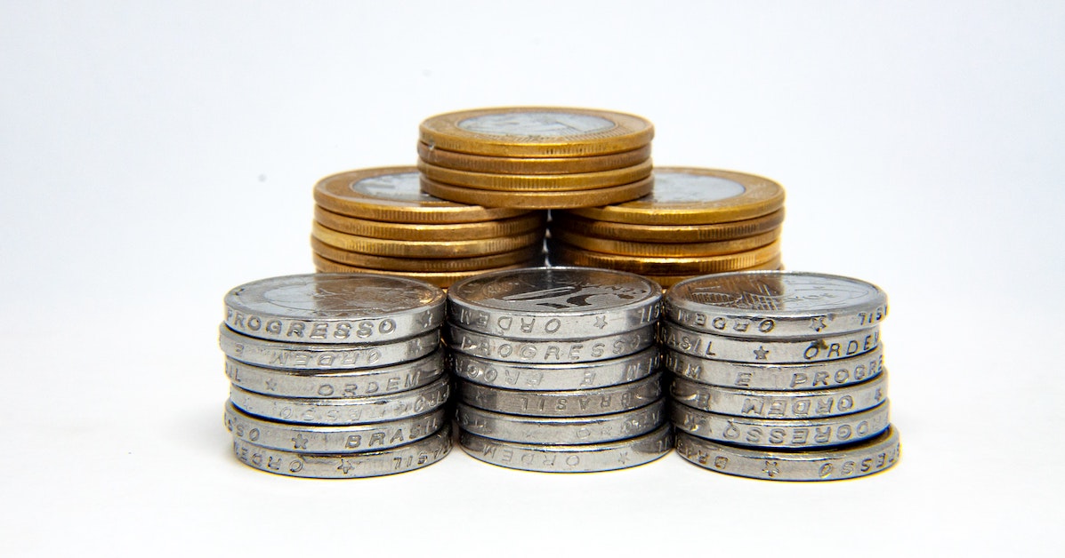 Moedas de um real e de cinquenta centavos empilhadas em uma mesa branca