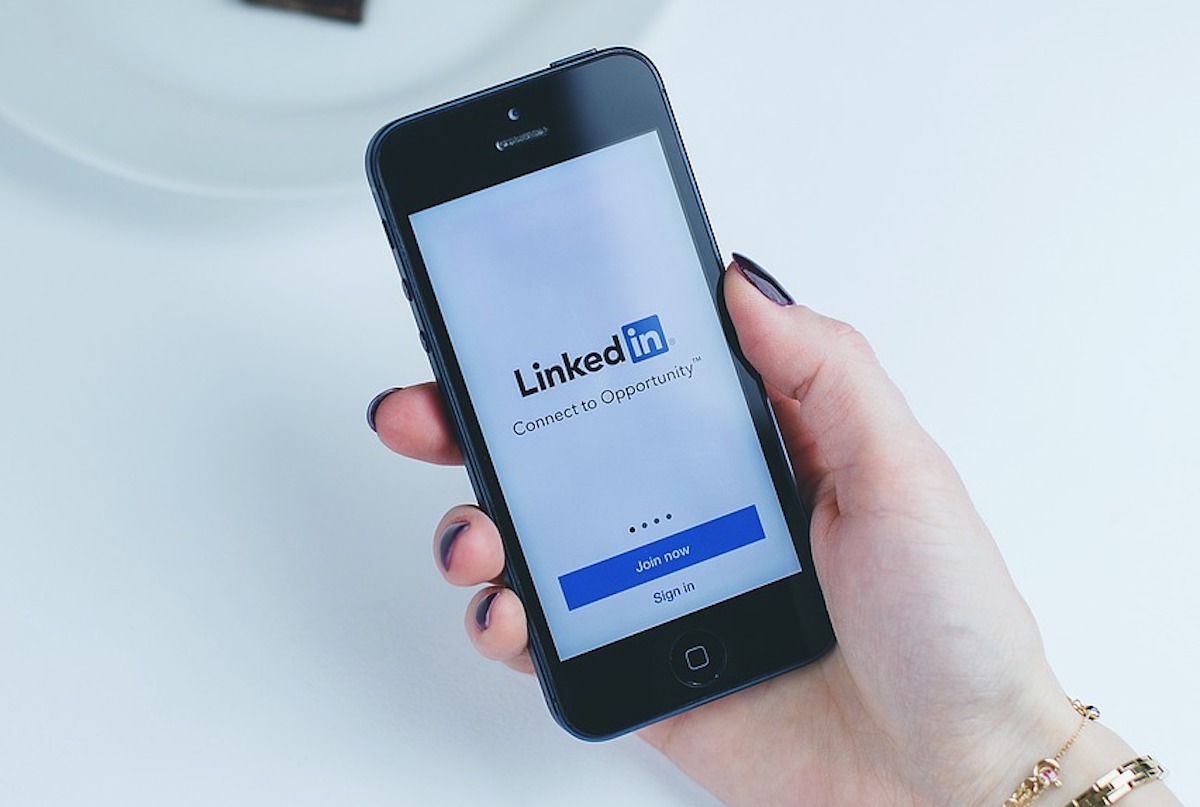 Mão feminina segurando celular com aplicativo do LinkedIn